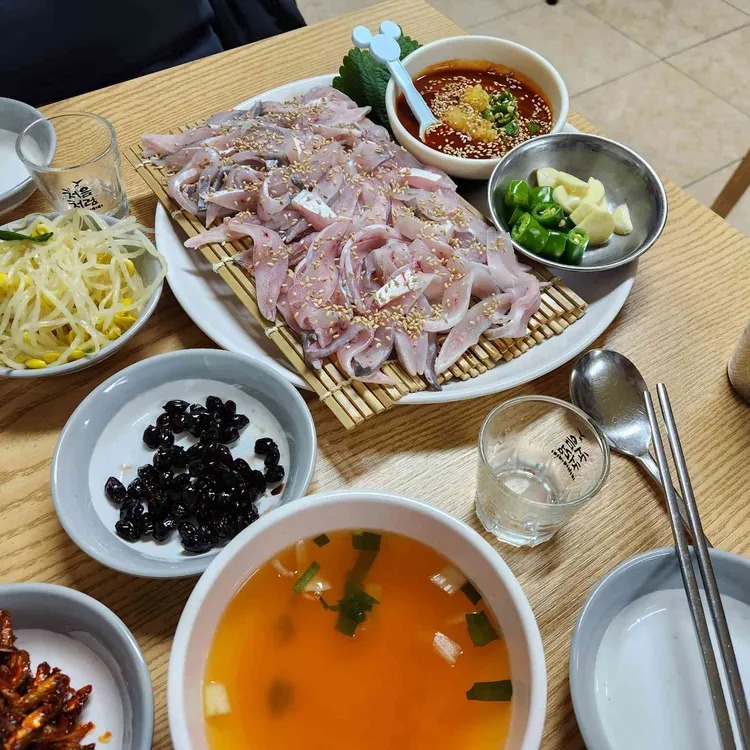 깨가 뿌려진 회와 국, 반찬들이 놓인 식탁